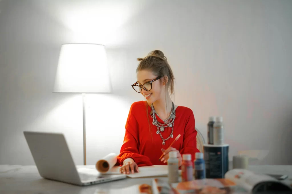 A young female business owner smiling while reviewing her product on a computer, likely pleased with the effectiveness of her remote staffing solutions.