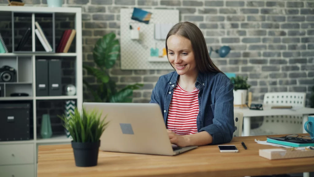 Happy girl smiling at her laptop, celebrating successfully landing her dream job with the help of a recruitment agency.
