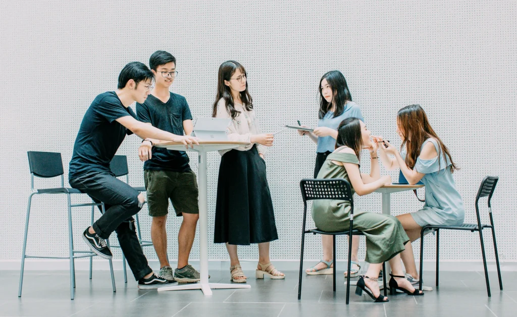 A diverse group of professionals sitting at tables in a well-lit office, engaged in work and discussions.