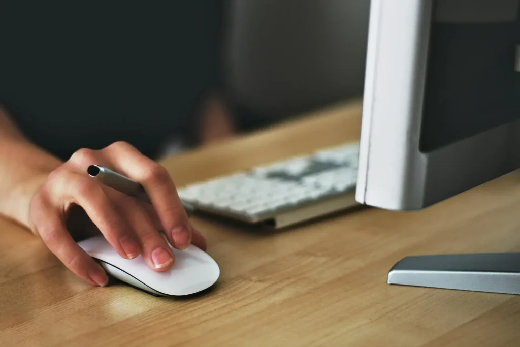 A person, an IT Portfolio Analyst, using a mouse on a desk to navigate and interact with a computer system efficiently.