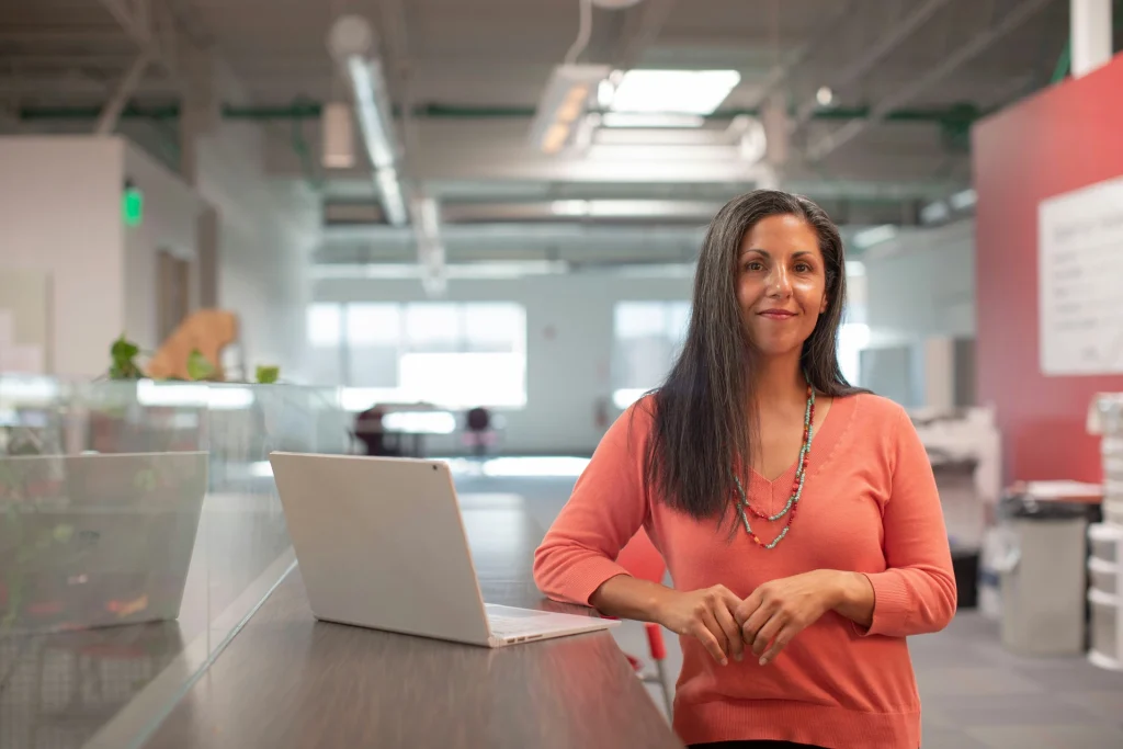 A woman standing in front of a laptop, focused and engaged in her work.